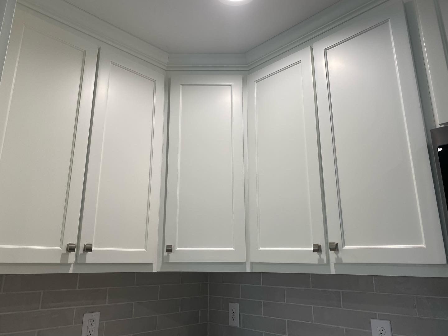 A kitchen with white cabinets and a gray tile wall.