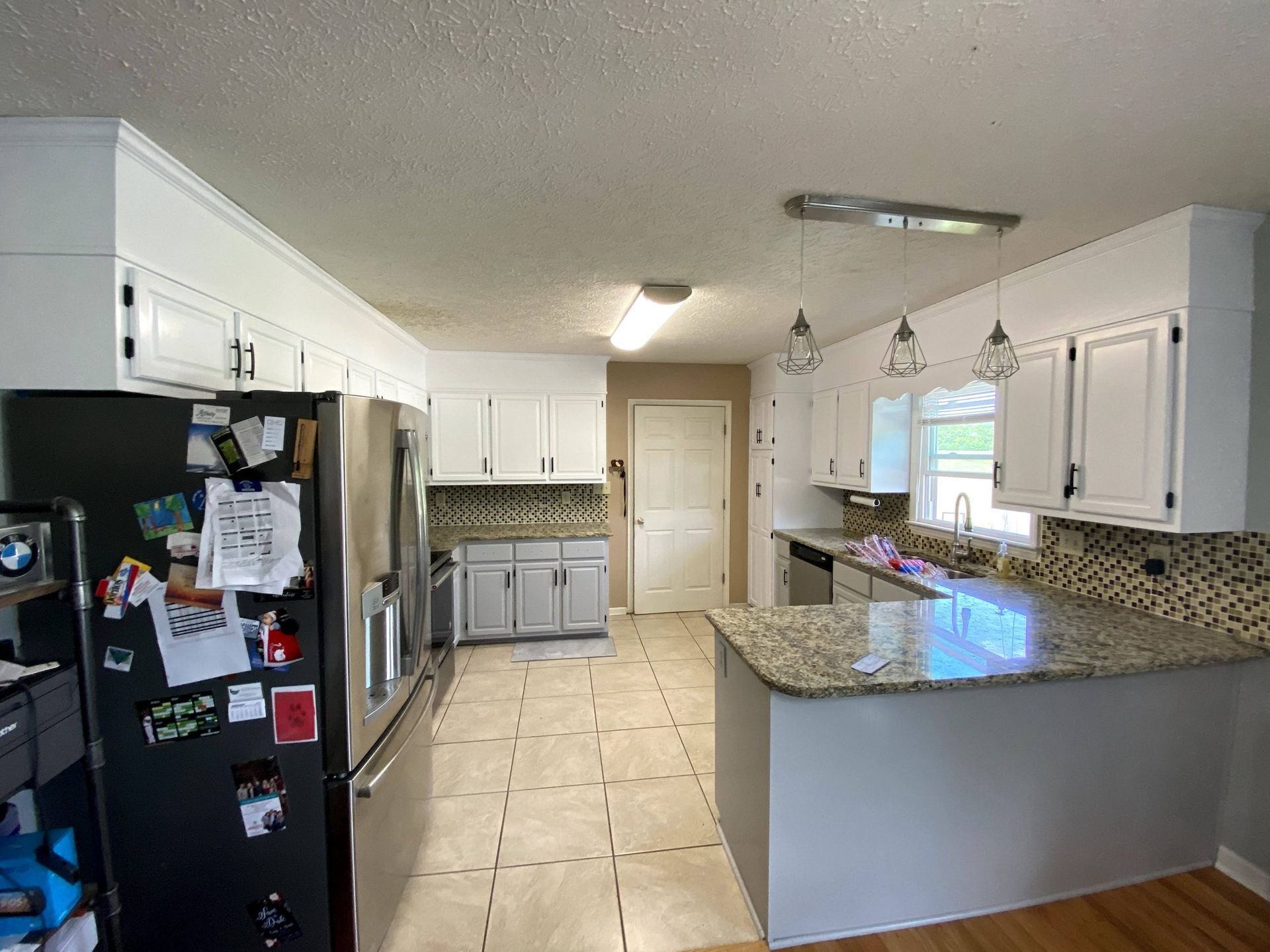 A kitchen with white cabinets , granite counter tops , stainless steel appliances and a black refrigerator.