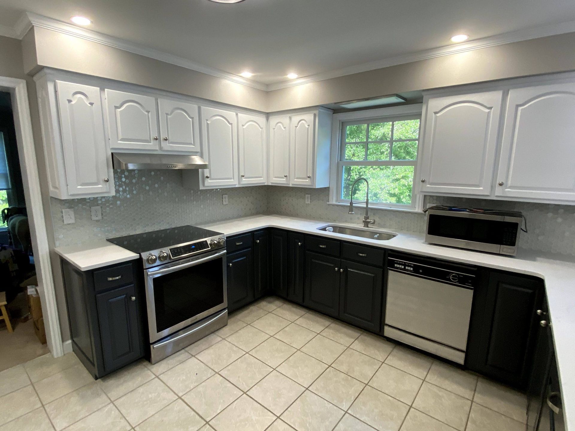 A kitchen with black cabinets , a stove , a sink , and a window.