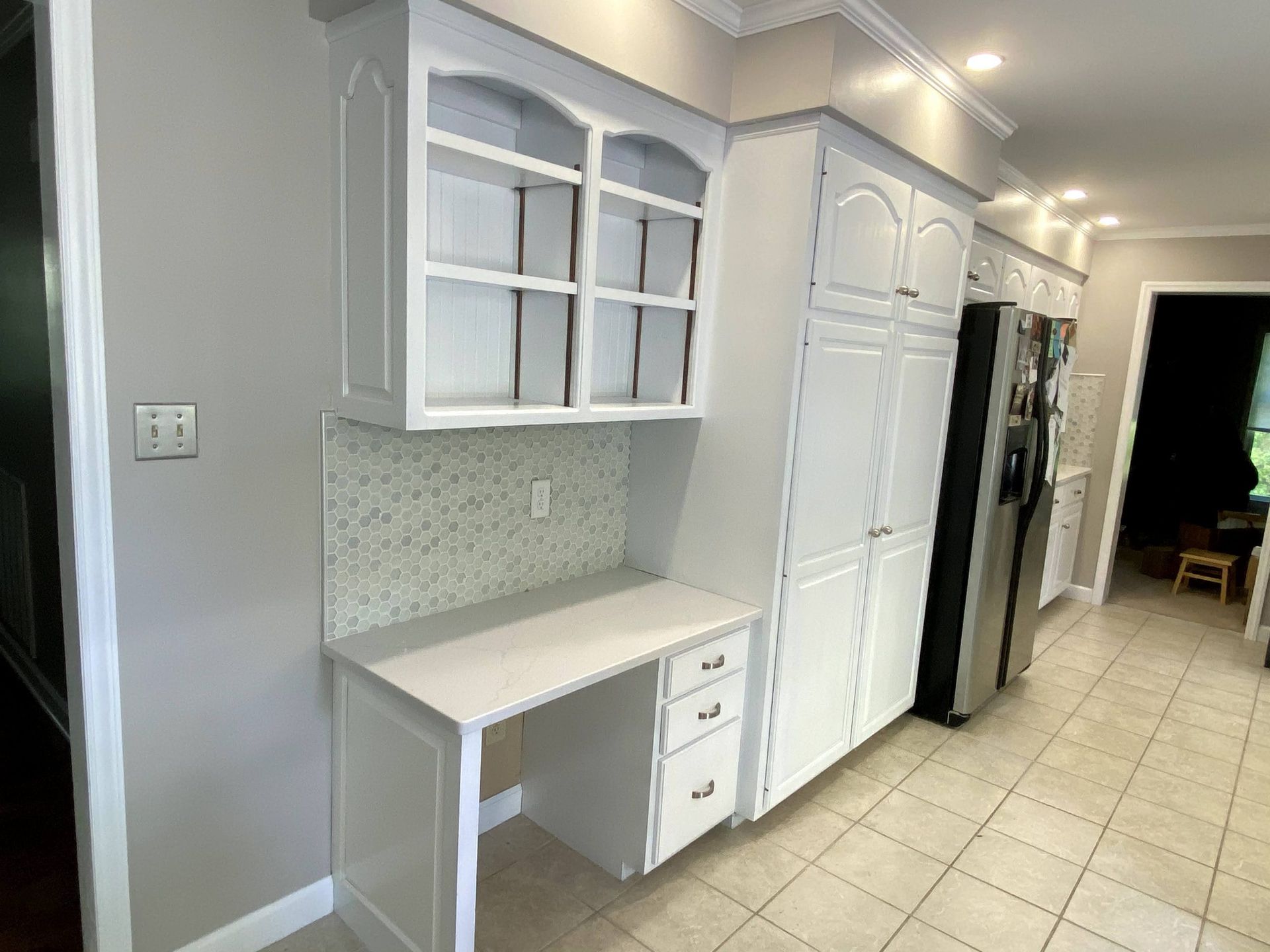 A kitchen with white cabinets , a desk and a refrigerator.