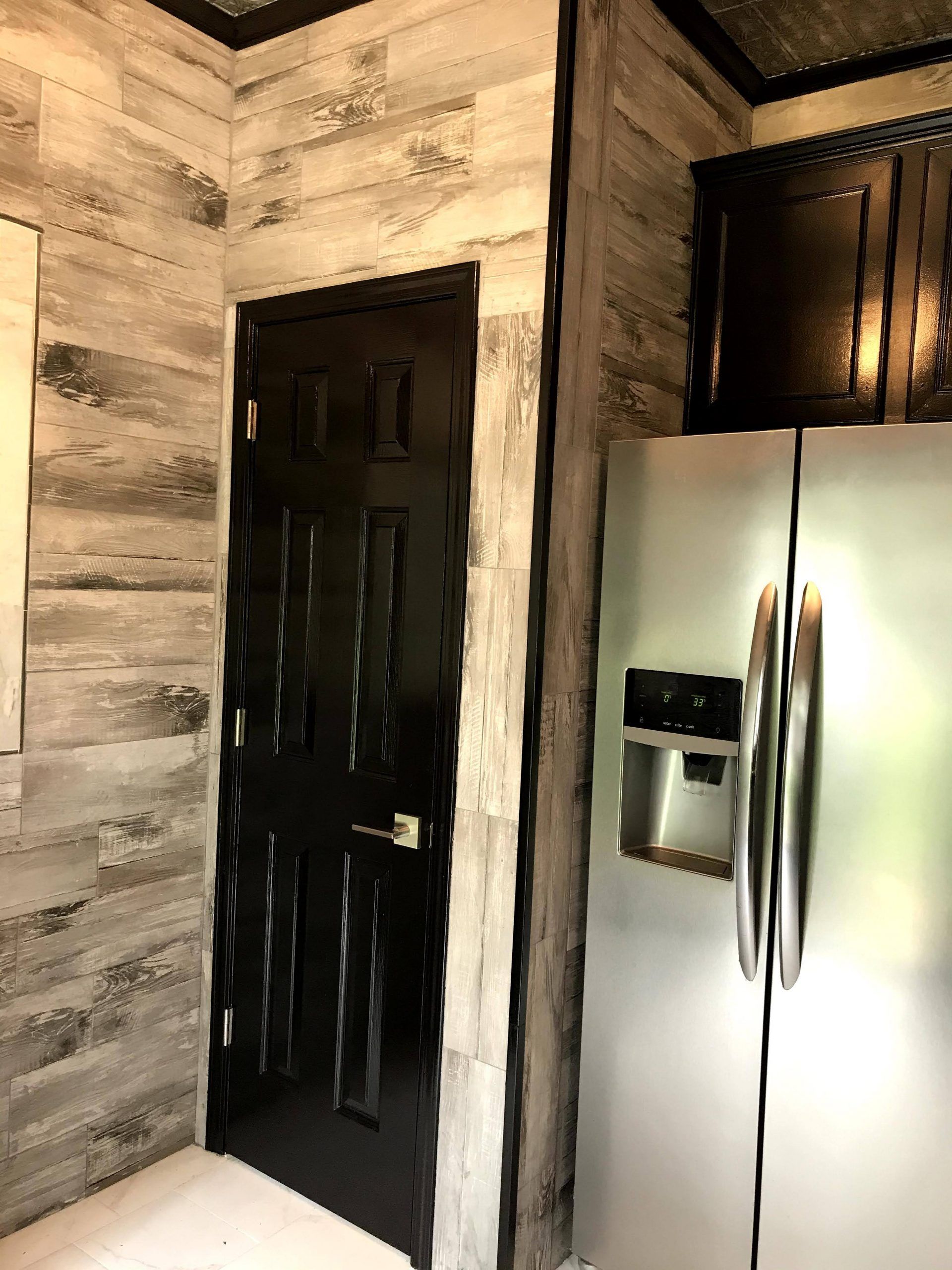 A kitchen with a refrigerator and a black door.