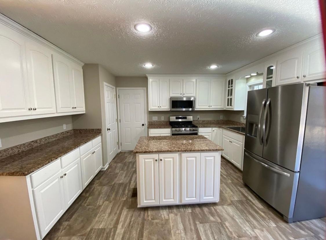 A kitchen with white cabinets , granite counter tops , stainless steel appliances and a large island.