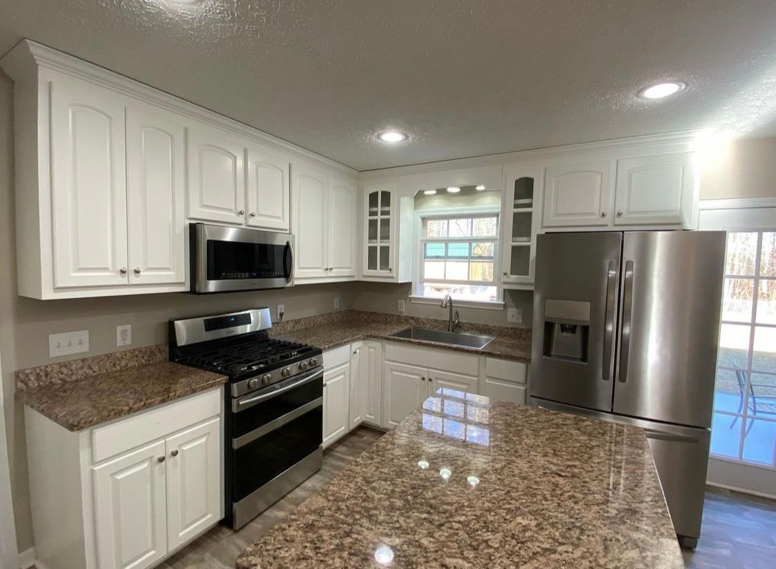 A kitchen with white cabinets , stainless steel appliances , granite counter tops and a large island.