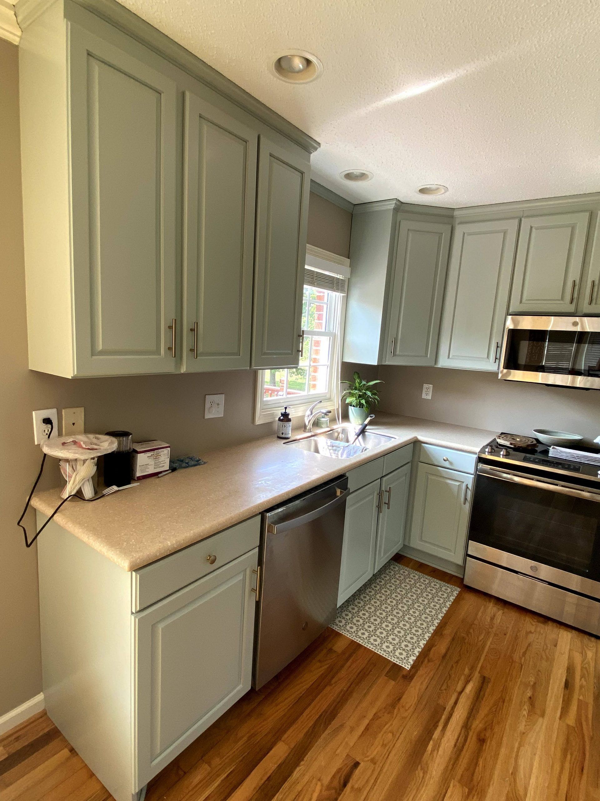 A kitchen with white cabinets , a stove , a dishwasher , and a window.
