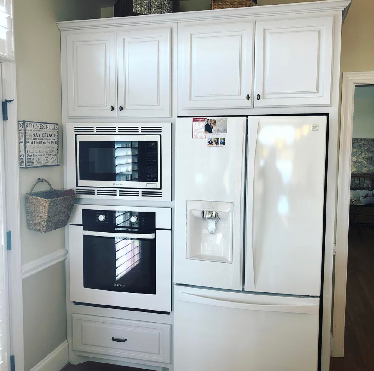 A kitchen with white cabinets and appliances including a refrigerator and microwave