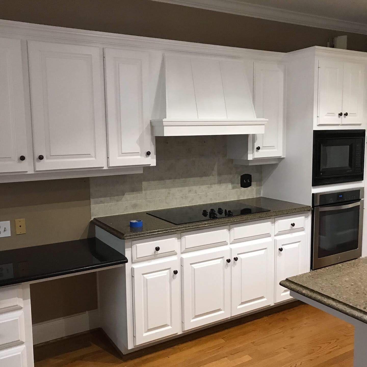 A kitchen with white cabinets , a stove , a microwave , and a sink.