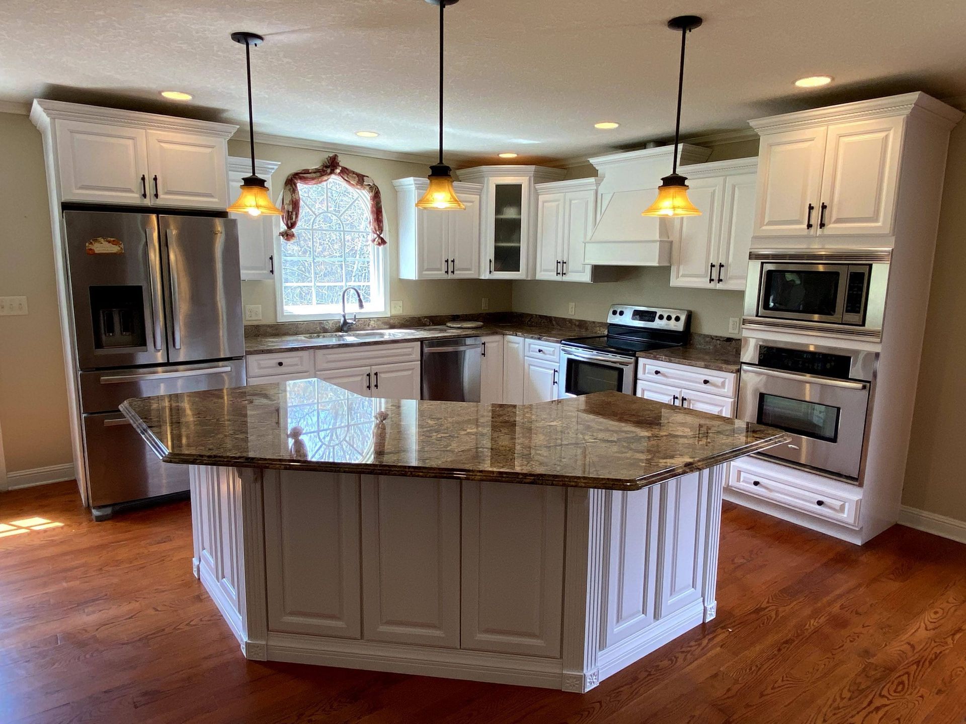 A kitchen with white cabinets , granite counter tops , stainless steel appliances and a large island.