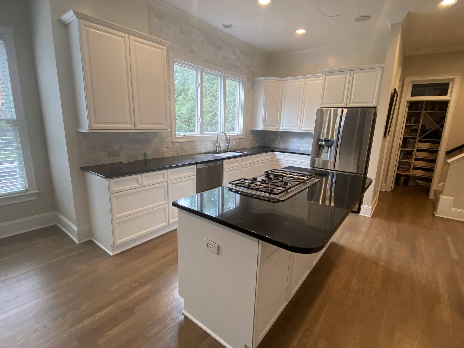 A kitchen with white cabinets , black counter tops , stainless steel appliances and a large island.