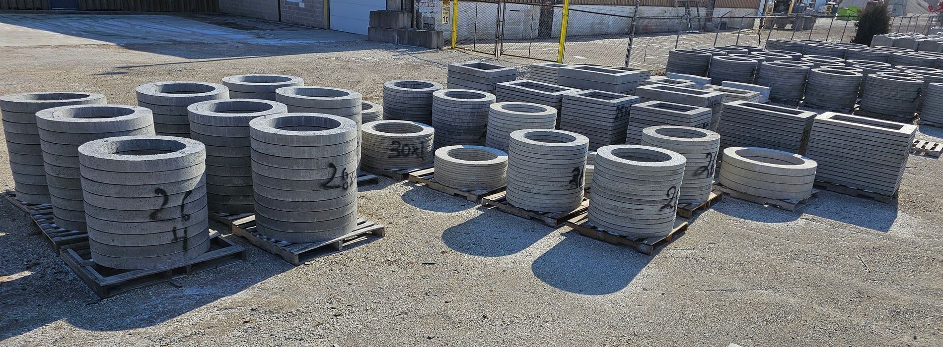 Stacked gray concrete pipe sections in a gravel yard outdoors
