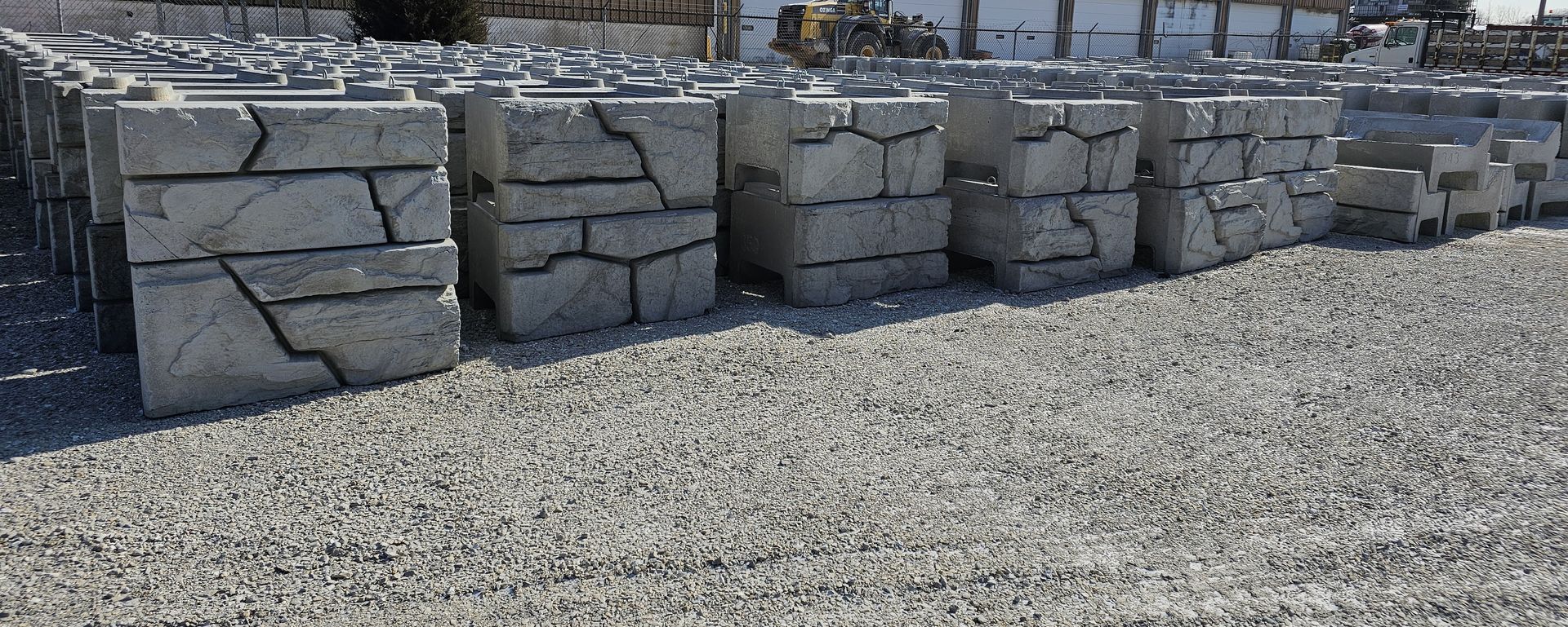 Rows of large gray stone blocks stacked on a gravel lot outdoors.