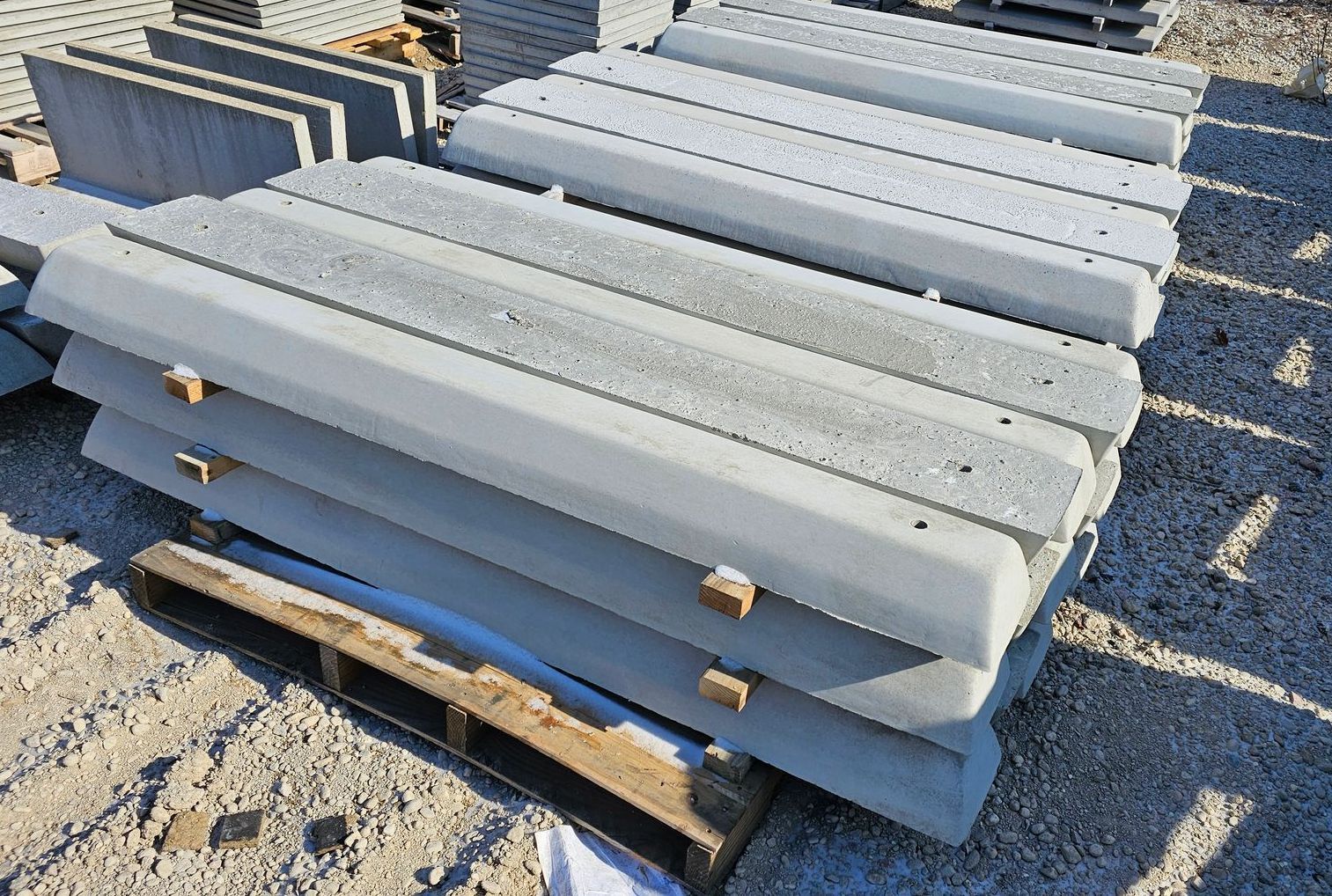 Stacked gray concrete beams on wooden pallets outdoors in bright sunlight.