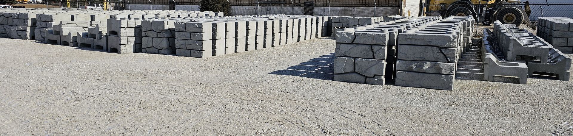 Stacks of gray cinder blocks and concrete pavers in an outdoor yard under bright sun.