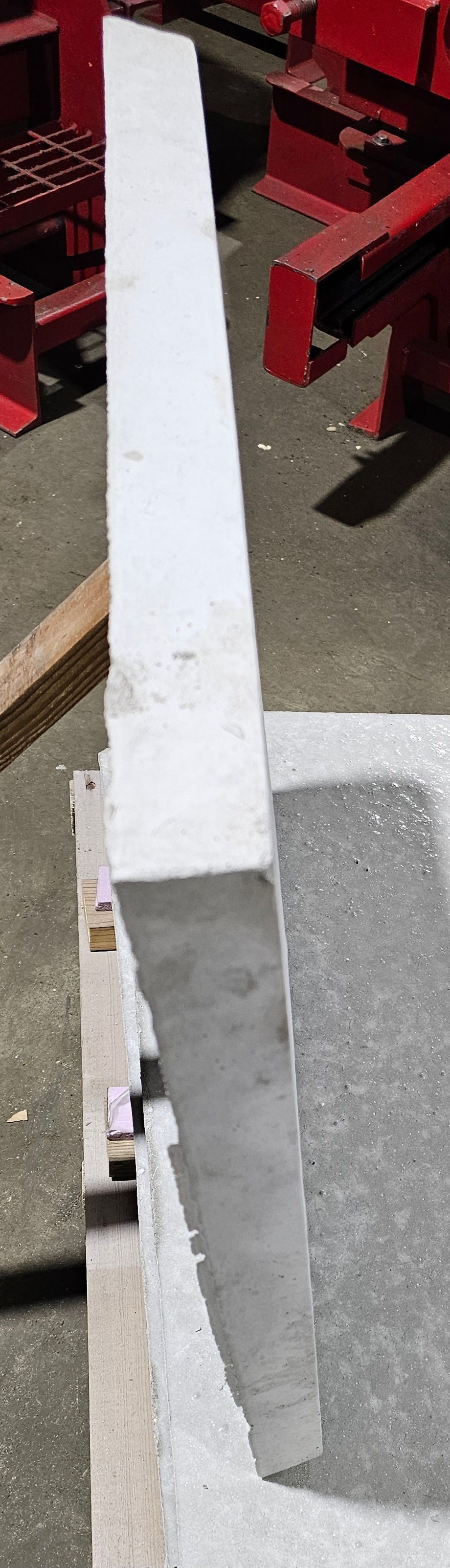 White metal beam leaning against a red structure on a concrete surface.