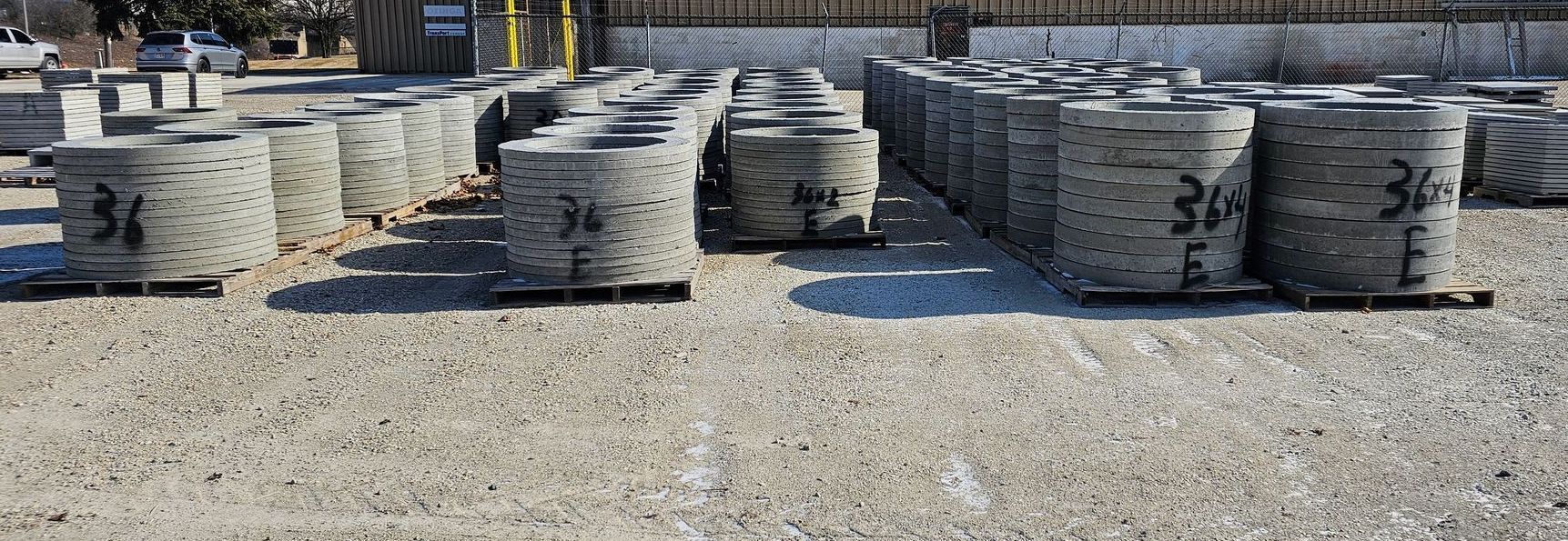 Stacks of gray stone blocks on pallets in an outdoor gravel yard under bright sunlight
