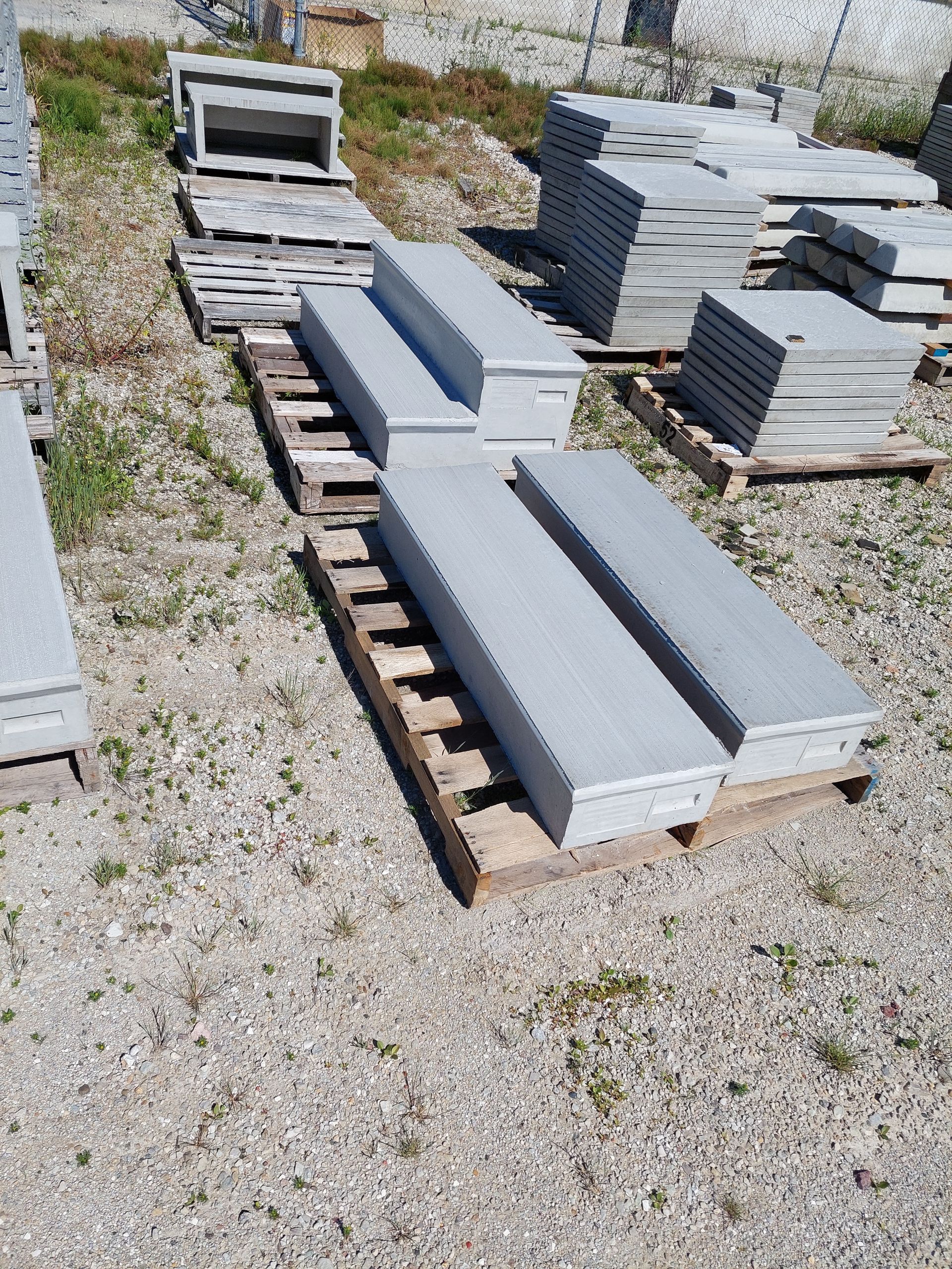 Stacks of gray concrete slabs on wooden pallets in a gravel yard.