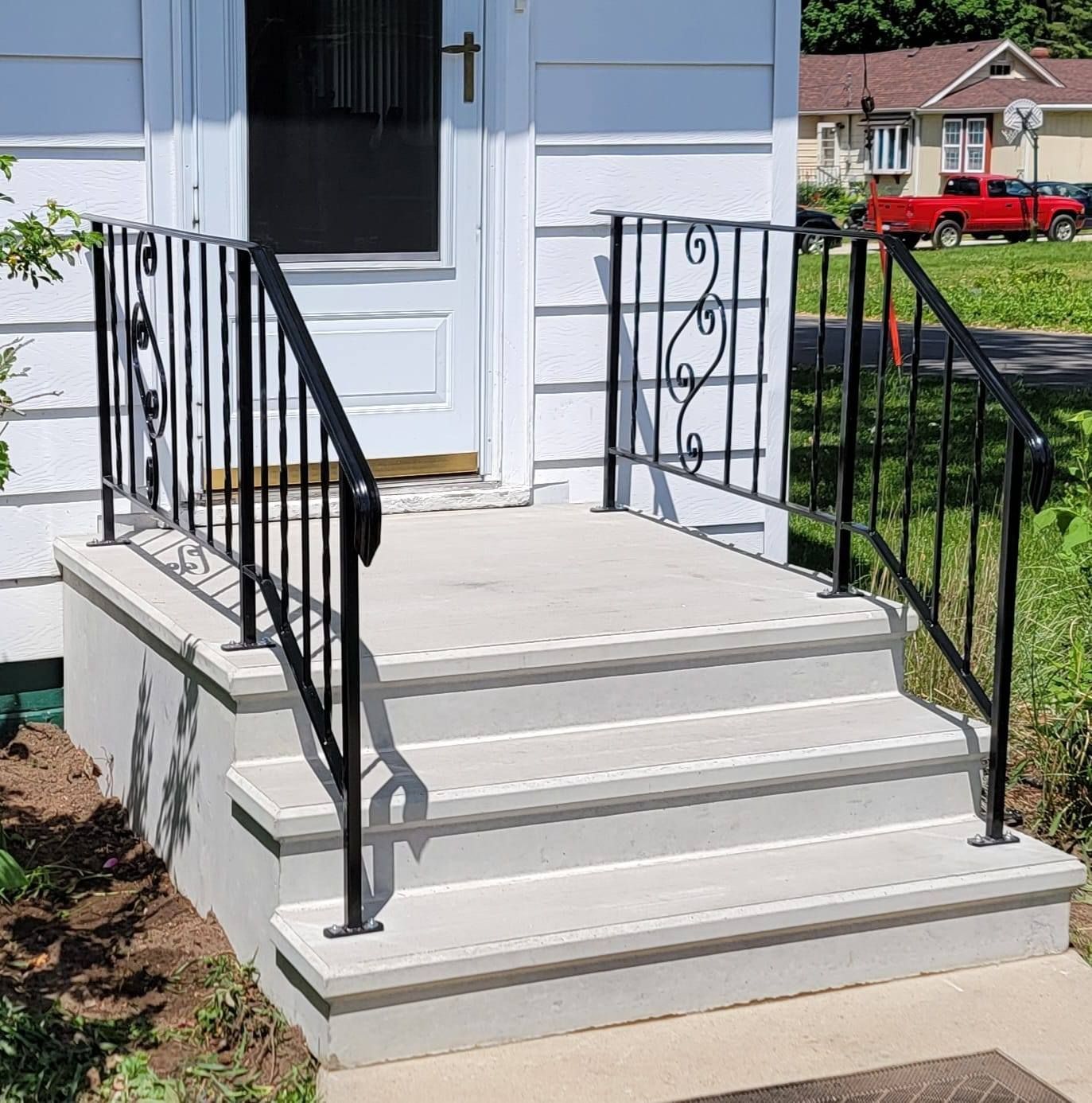 Front porch with concrete steps, black railings, and a white door on a house under construction