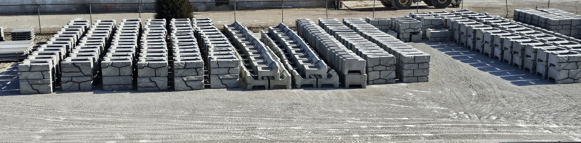 Stacks of gray concrete blocks arranged in rows on a gravel lot outdoors