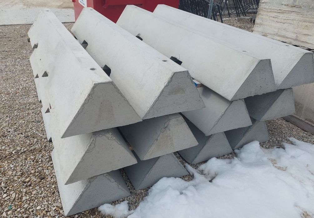 Stacked gray concrete barriers on gravel beside snow