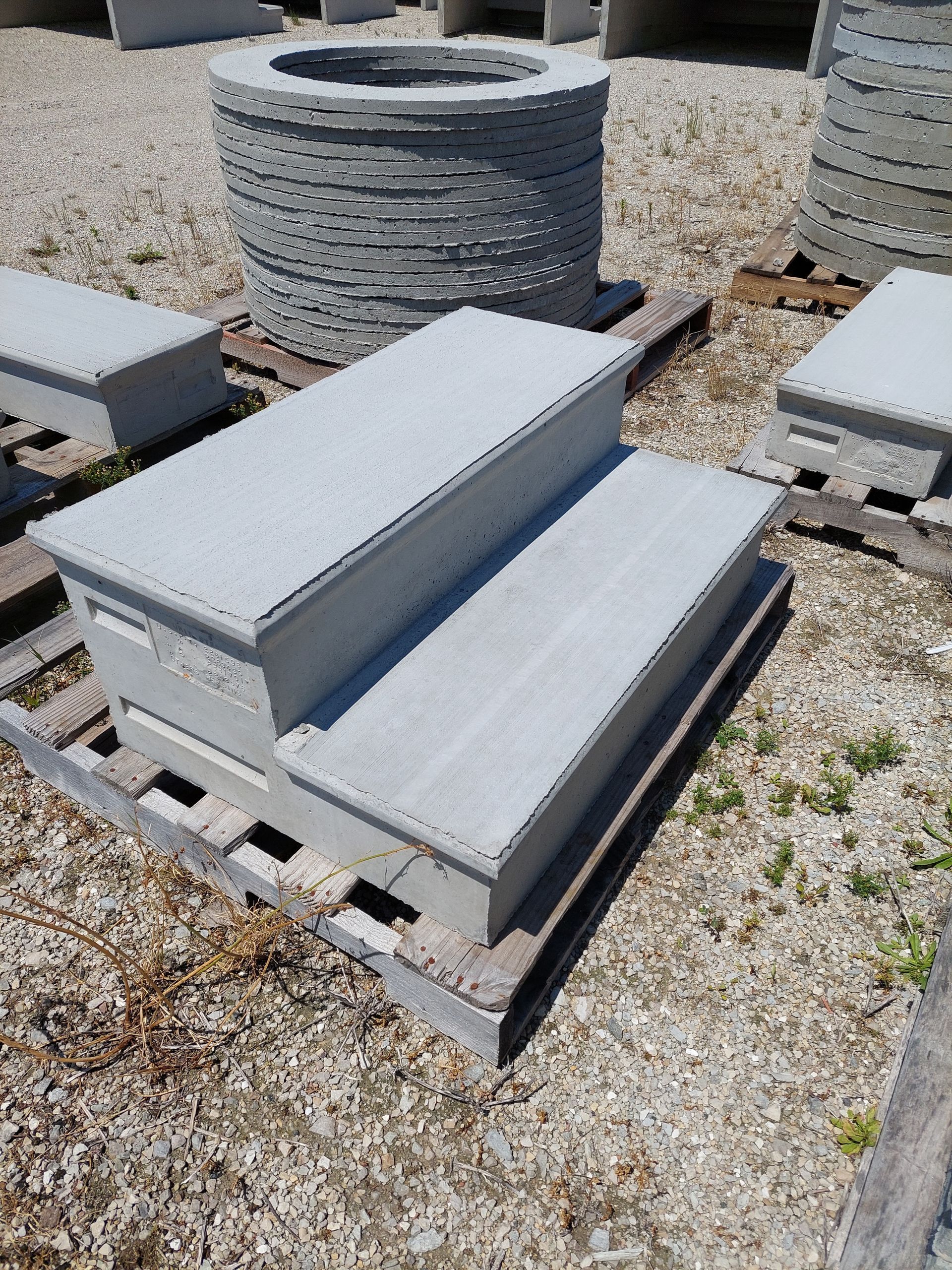 Stacked gray concrete steps on a pallet in an outdoor gravel yard.