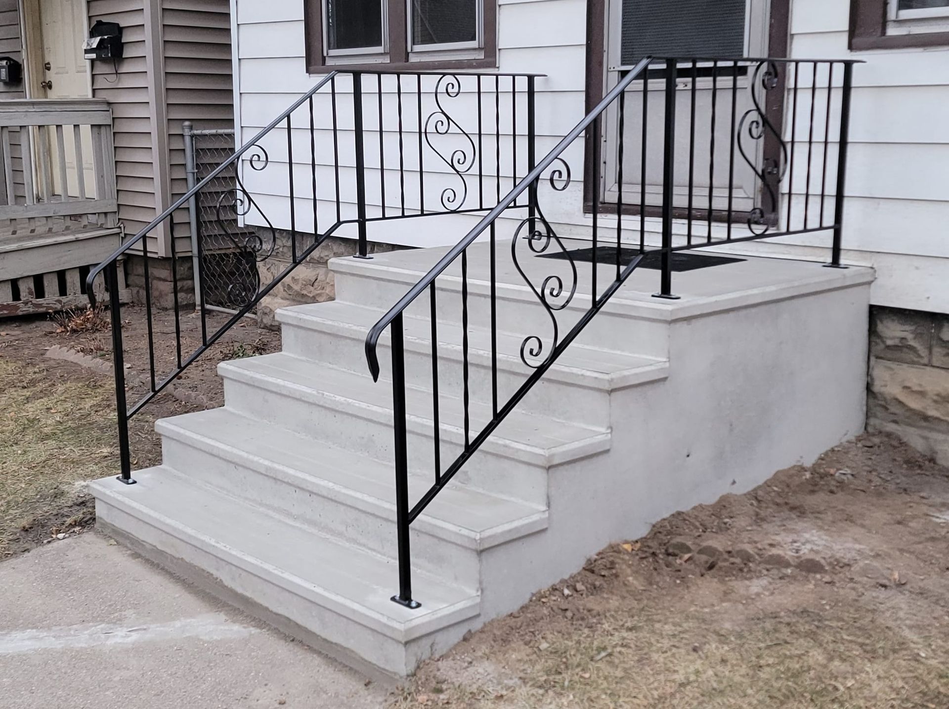 Concrete porch steps with black metal railings leading to a white front entrance.