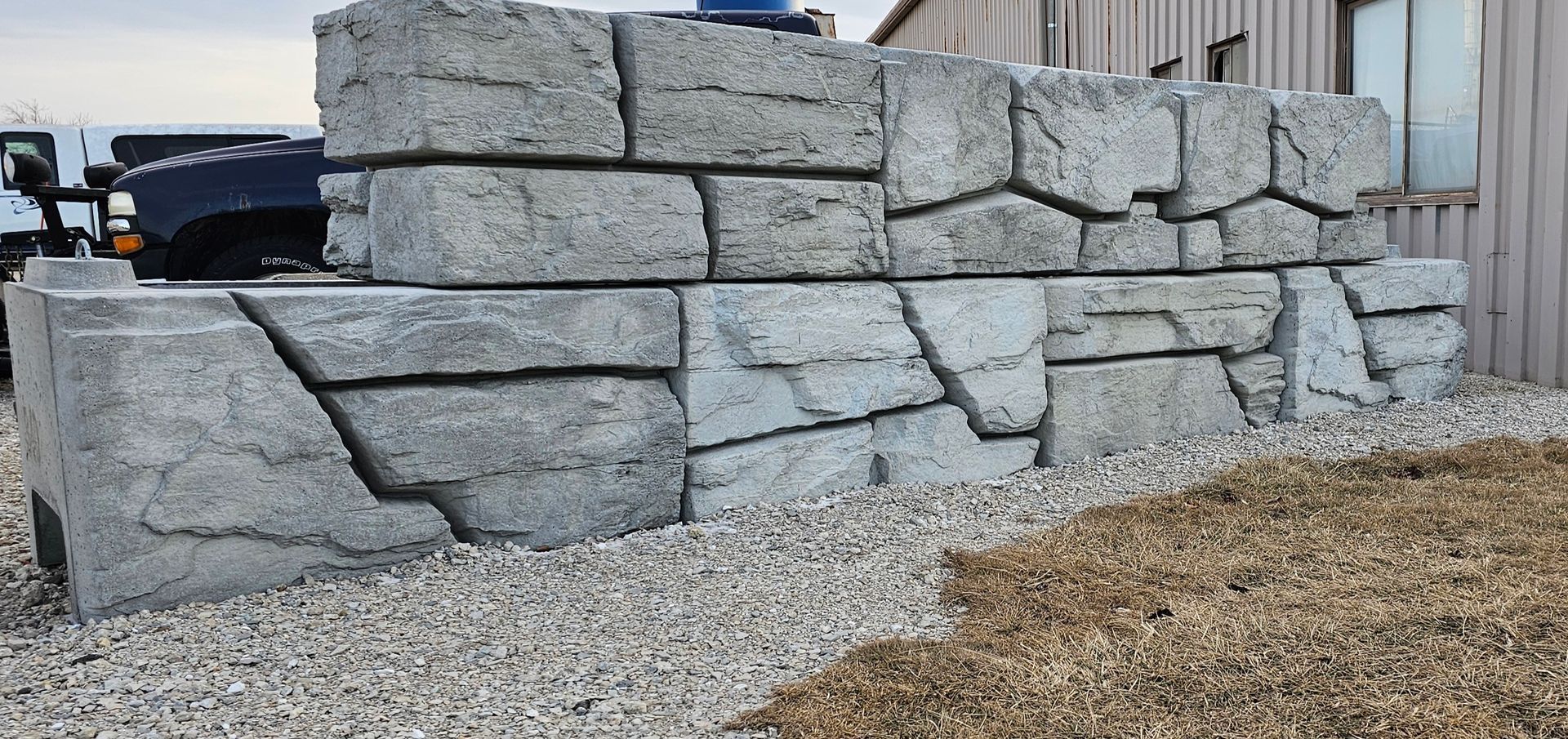 Stacked gray stone retaining wall on gravel beside a building site