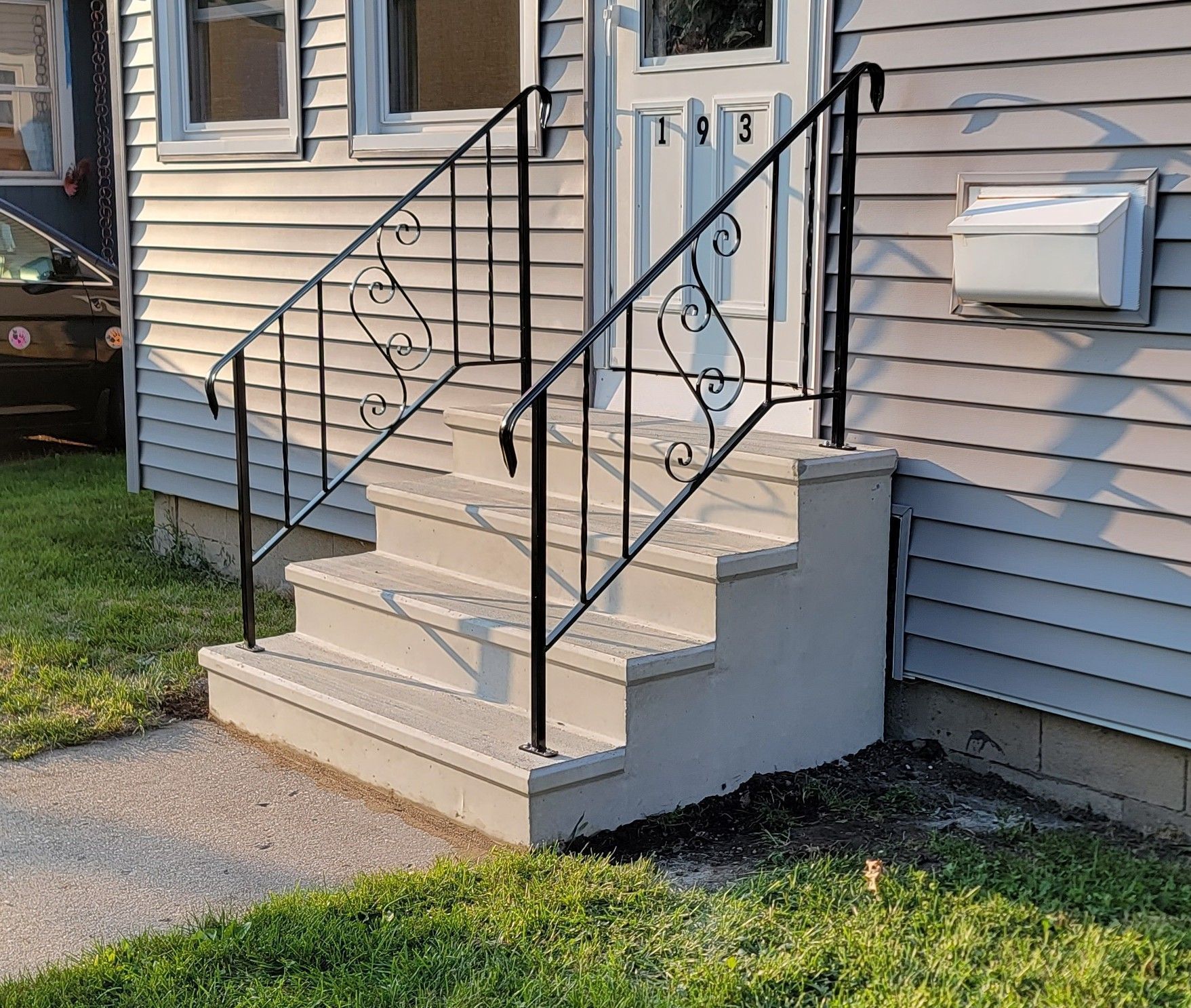 Front steps of a house with beige siding, black railings, and a white mailbox