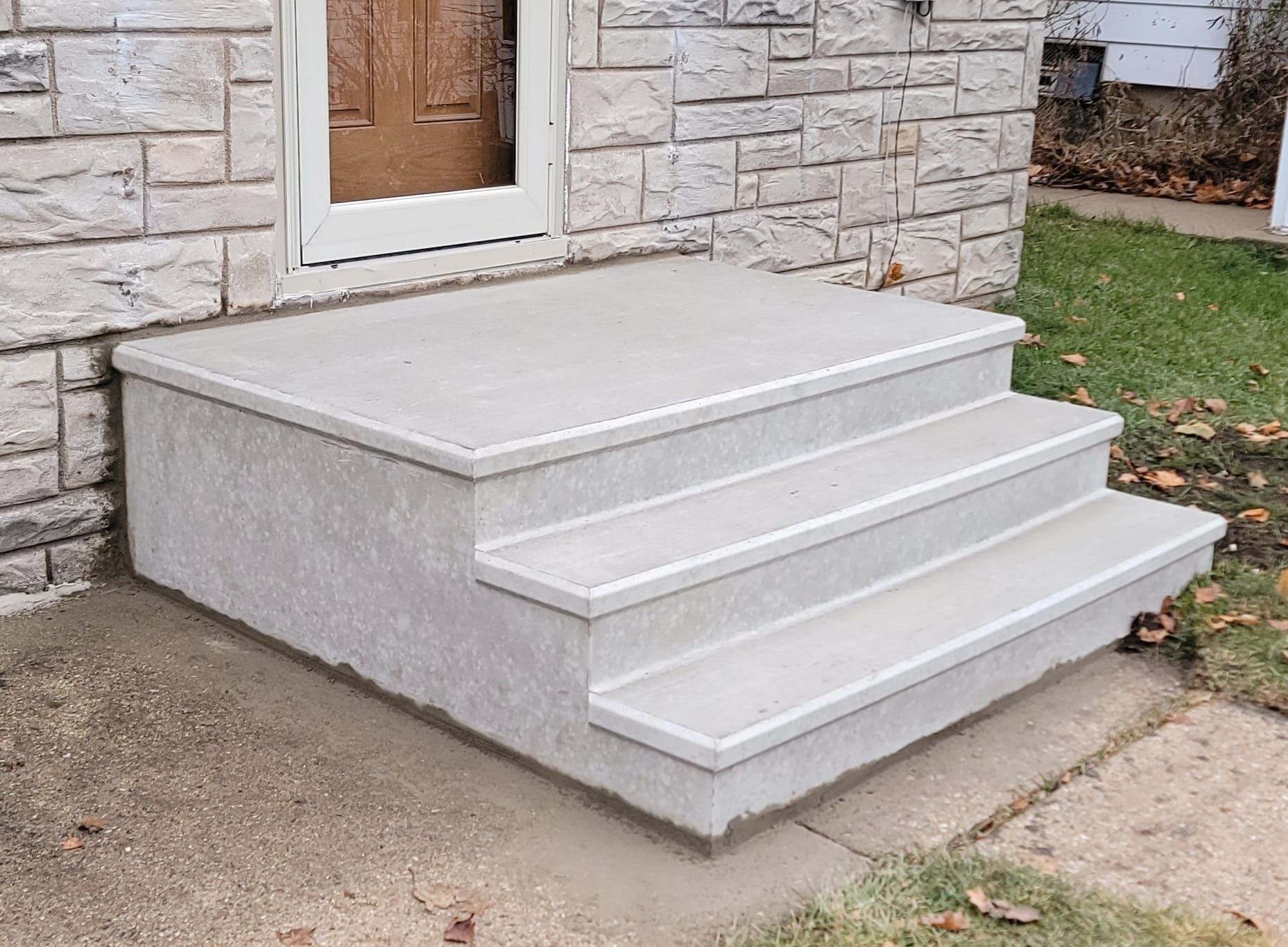 Concrete front steps with a small landing leading to a stone house door