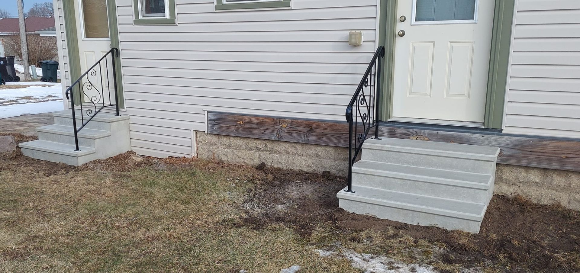 Front of a house with two small porches and steps leading to doors, with patchy grass in front.