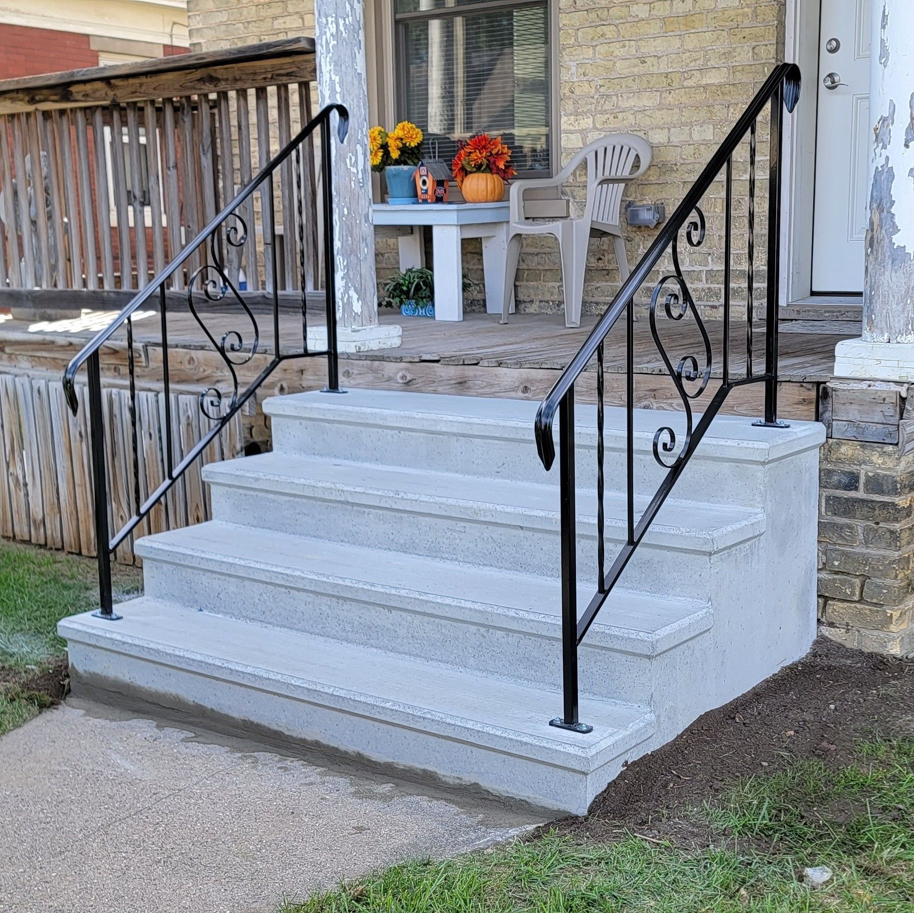 Front porch stairs with black railings, white steps, and autumn decorations on a small table.