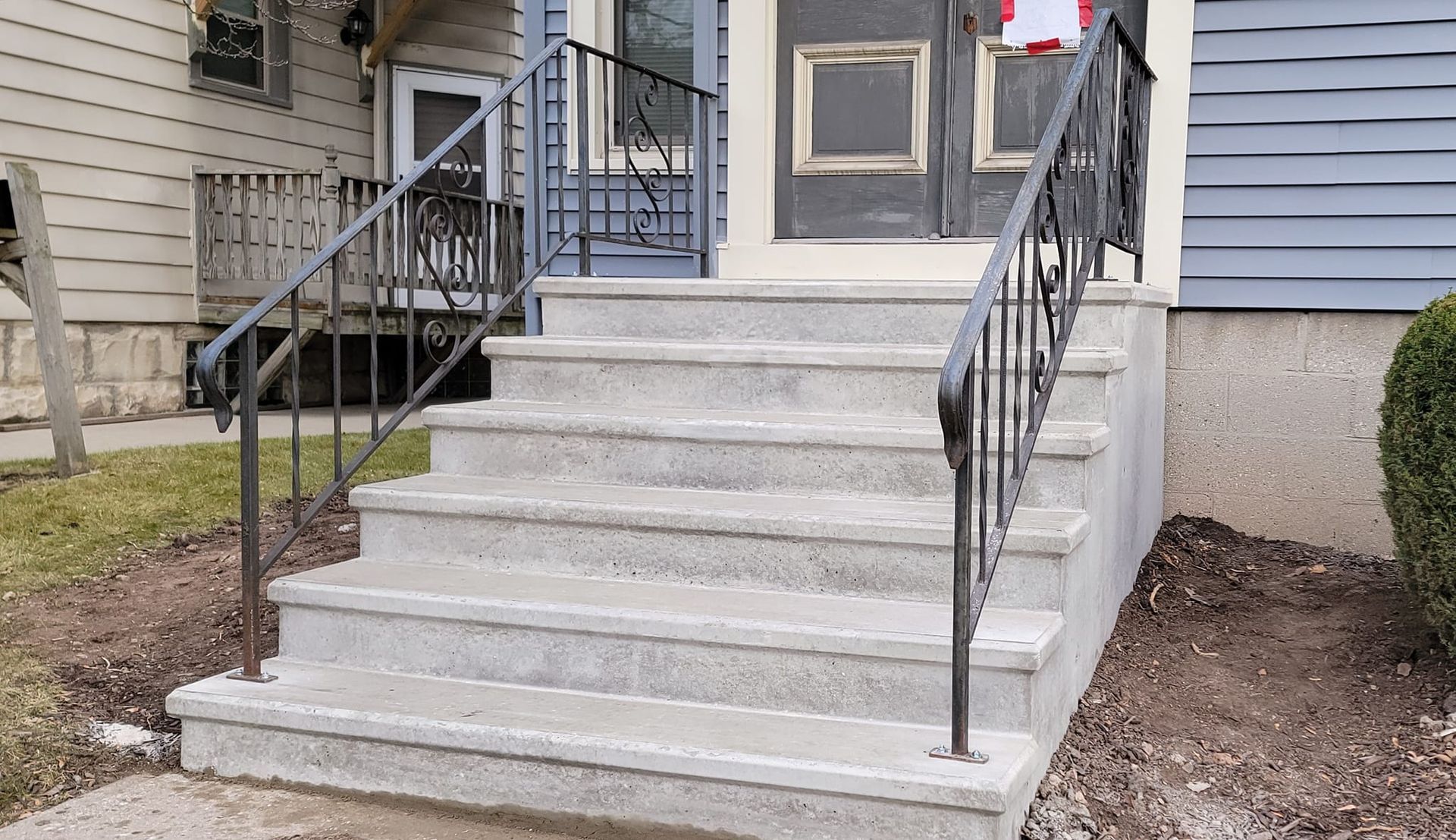 Front steps leading to a house entrance with black metal railings and a concrete landing.