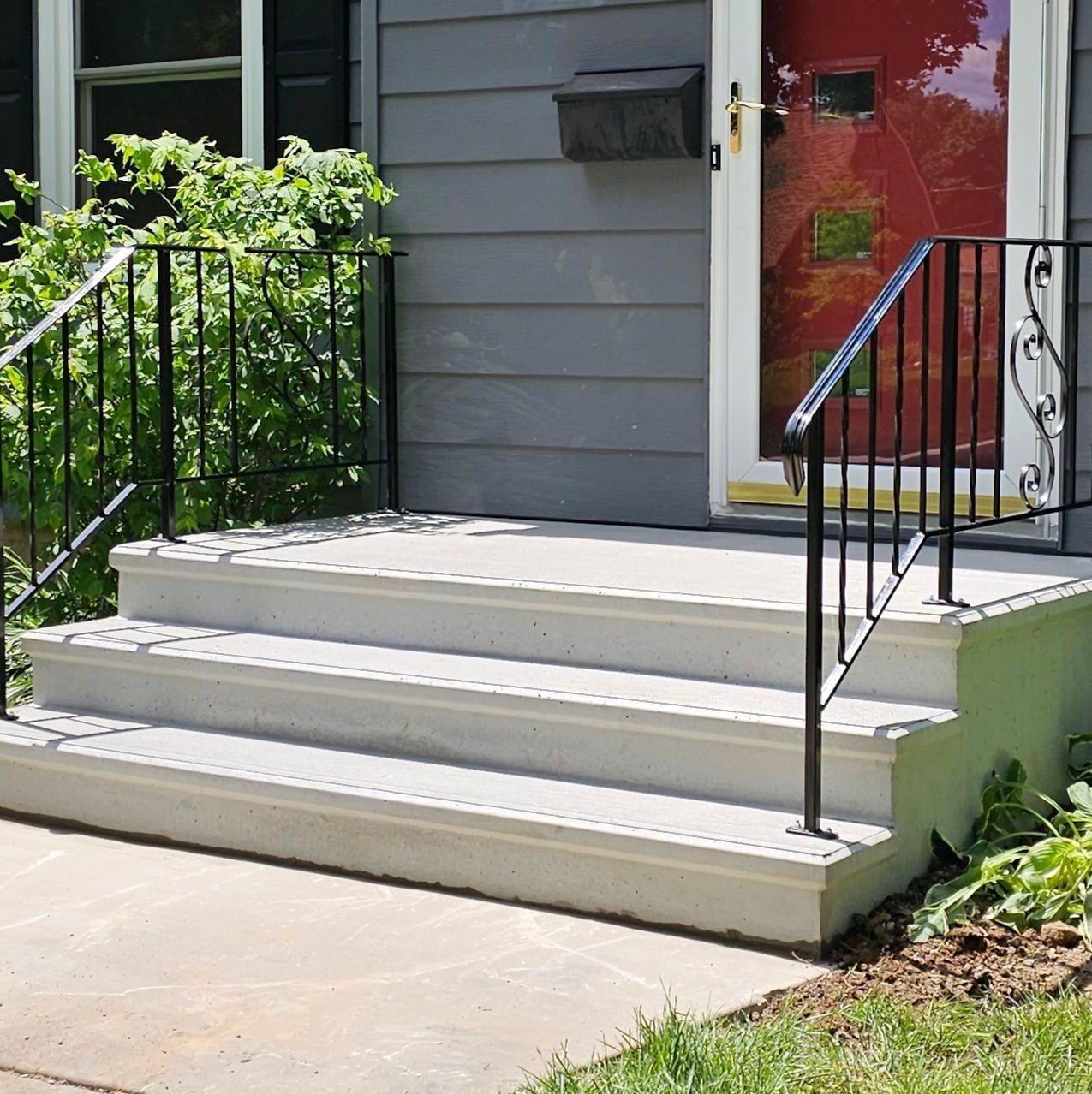 Front porch with concrete steps, black railings, and a red front door on a house.