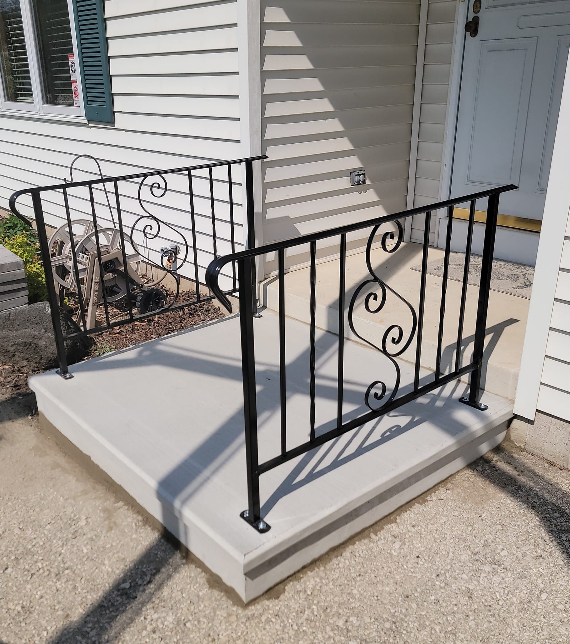 Concrete porch ramp with black metal railings beside a house entrance