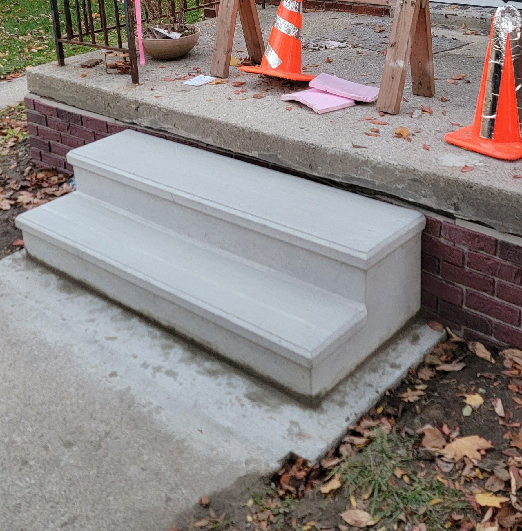 White concrete step ramp beside a brick porch, with orange cones on the top landing