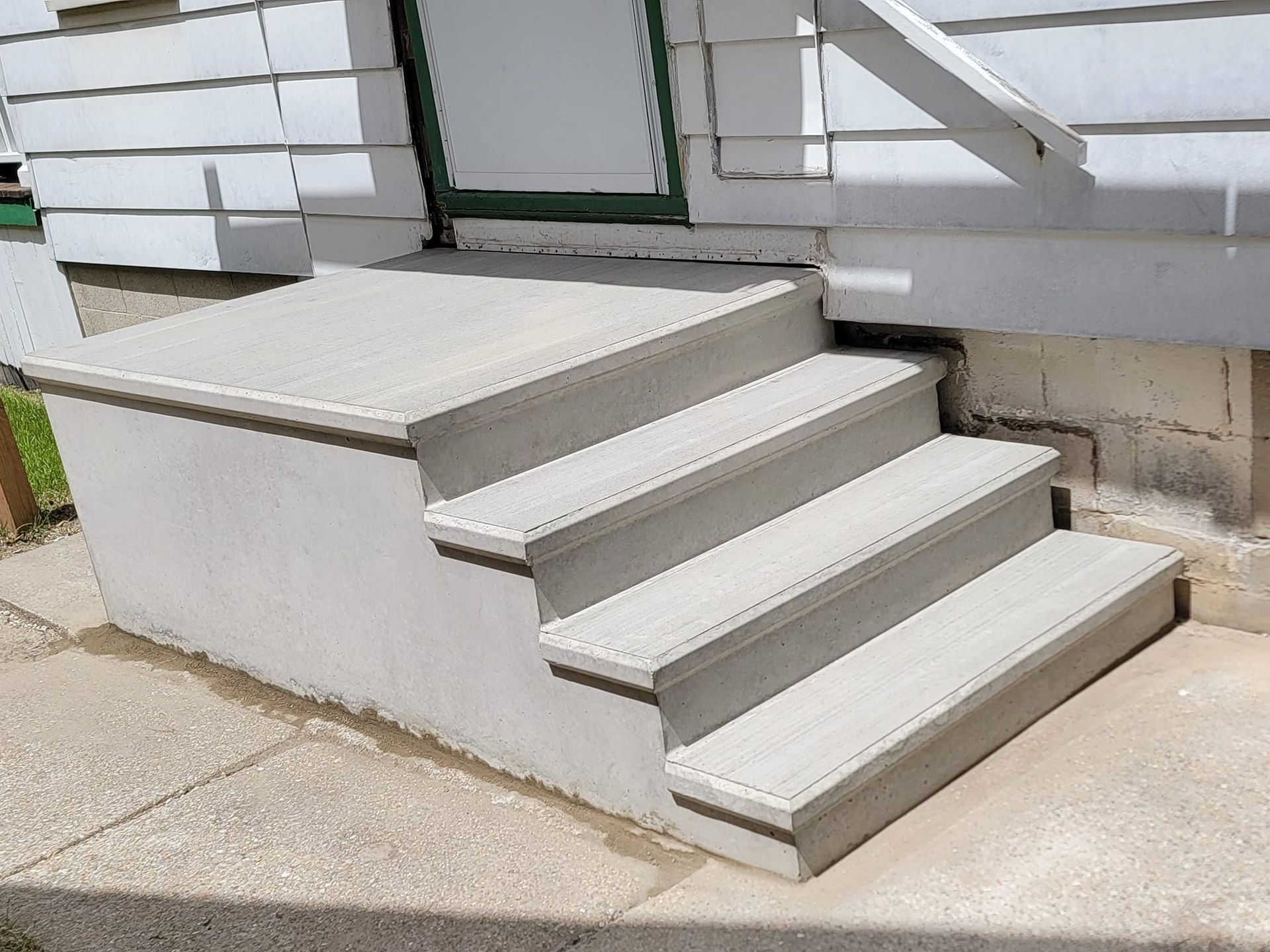Concrete stairs leading to a green door entrance with white siding and a small landing.