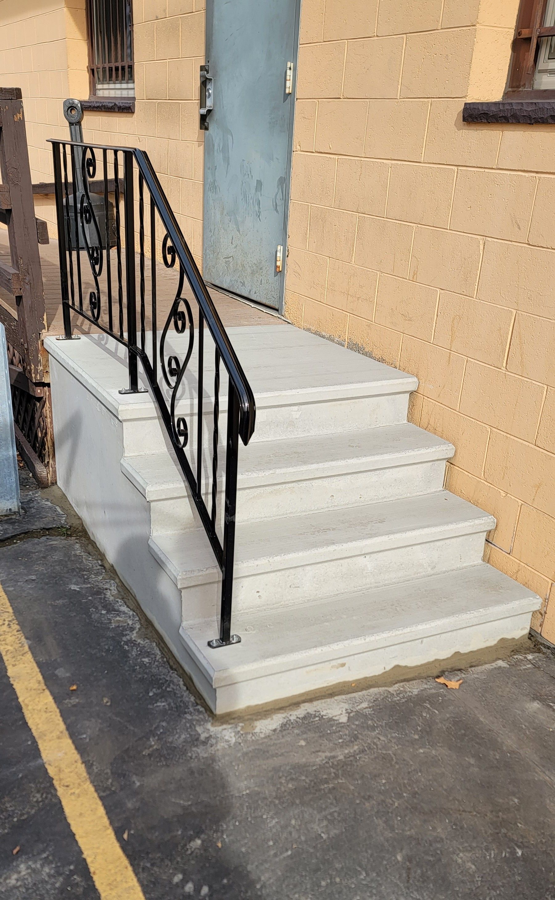 White concrete steps with black metal railings leading up to a blue door on a tan building.