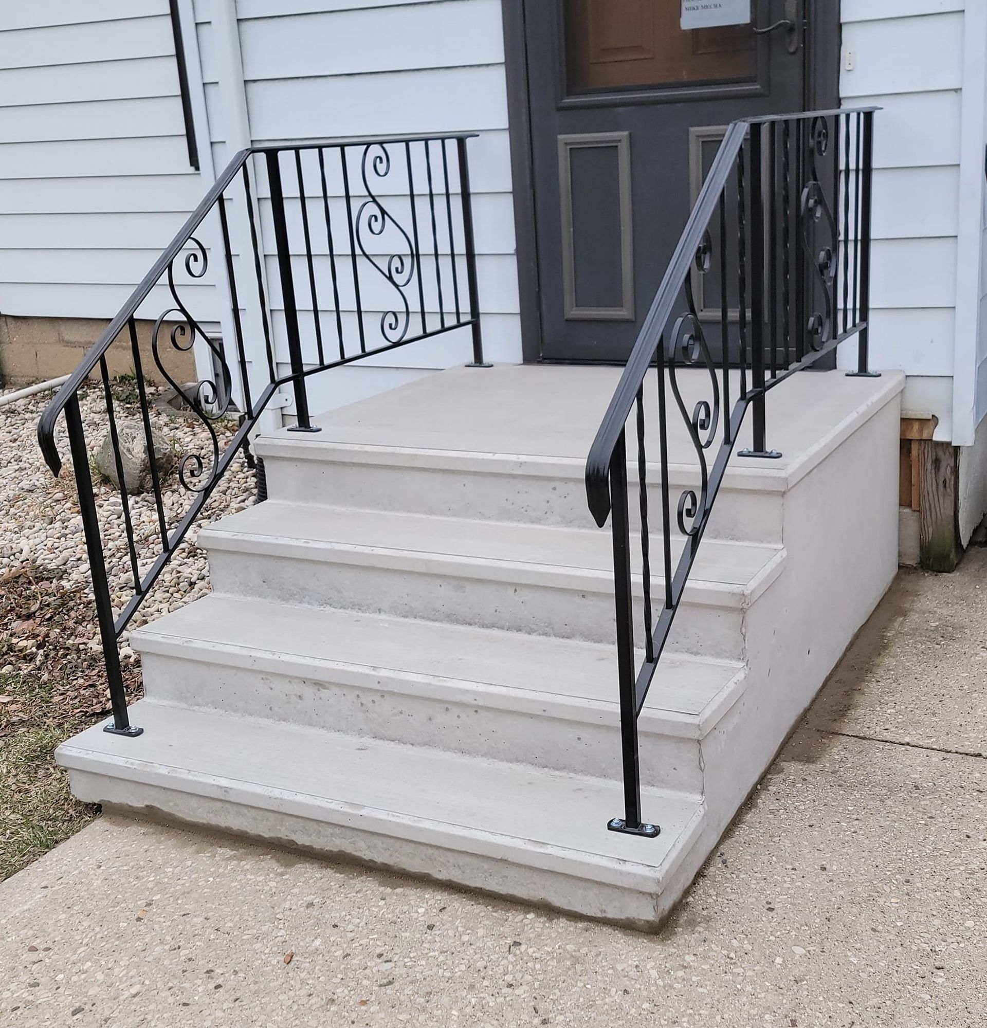 Front porch steps with black metal railings leading to a gray front door