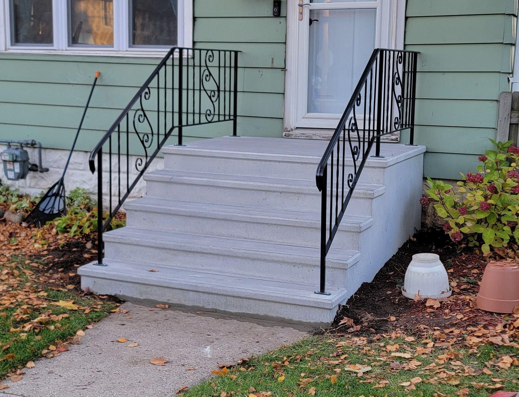 Front porch steps with black railings and a concrete ramp beside a house, bordered by fallen leaves.