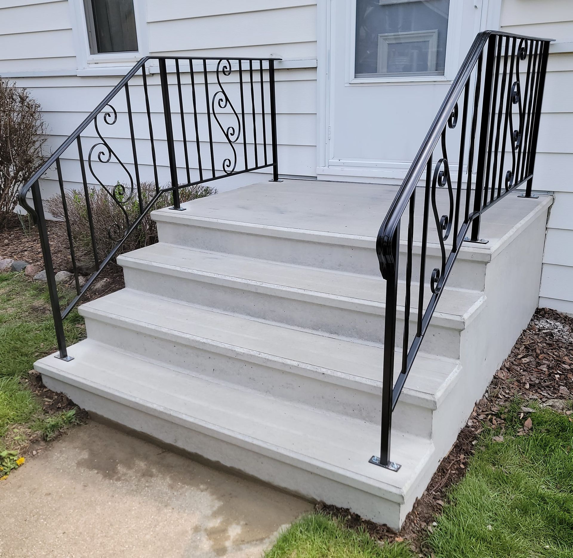 Front steps with white concrete stairs and black wrought-iron railings leading to a house entrance