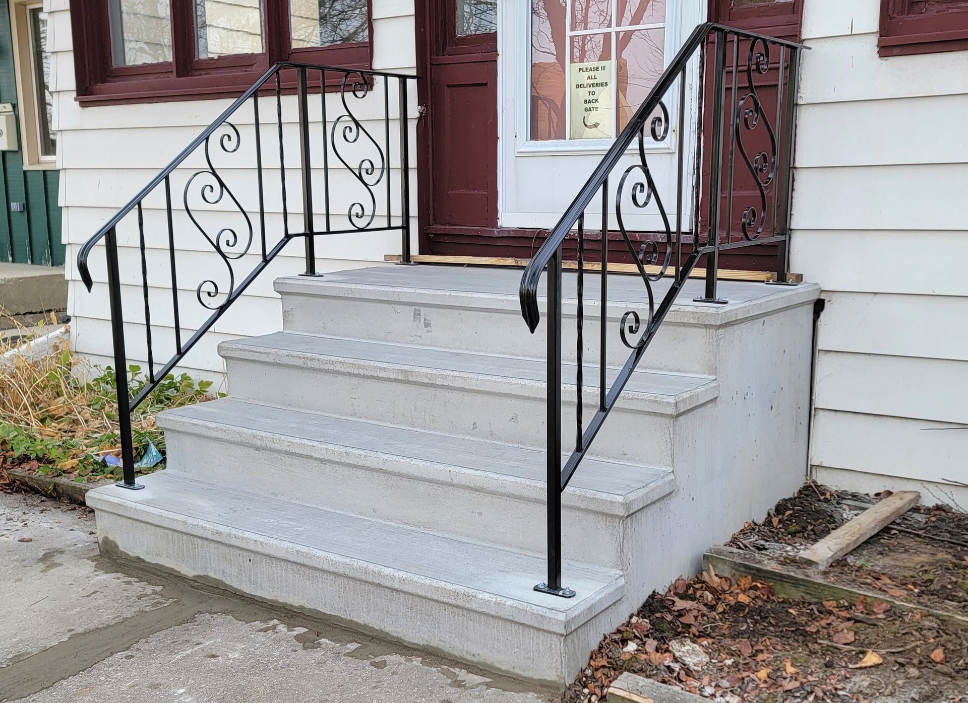 Front steps with gray concrete stairs and black wrought-iron railings leading to a white house entrance