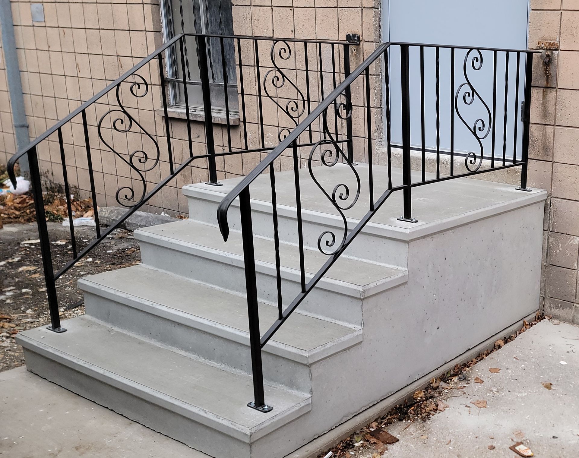 Concrete porch stairs with black wrought-iron railings beside a brick building