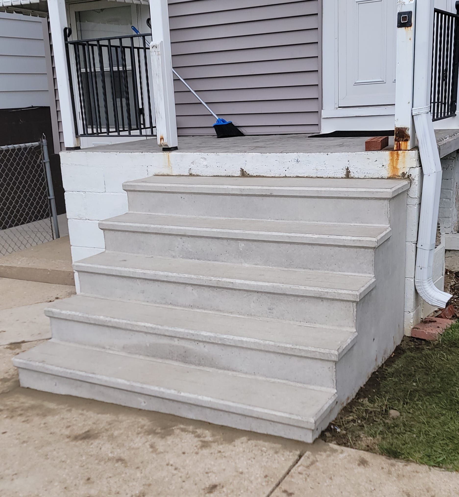 Front steps and porch of a house, with a blue broom resting on the landing.