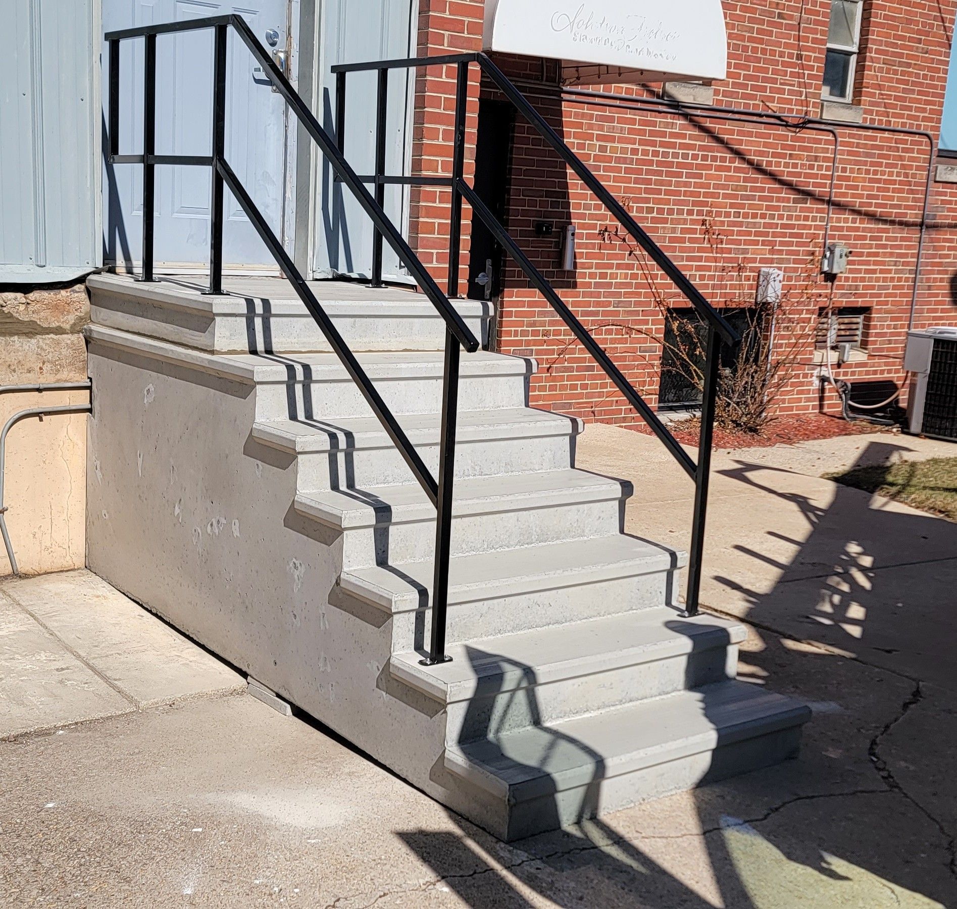 Concrete outdoor stairway with black handrails beside a brick building
