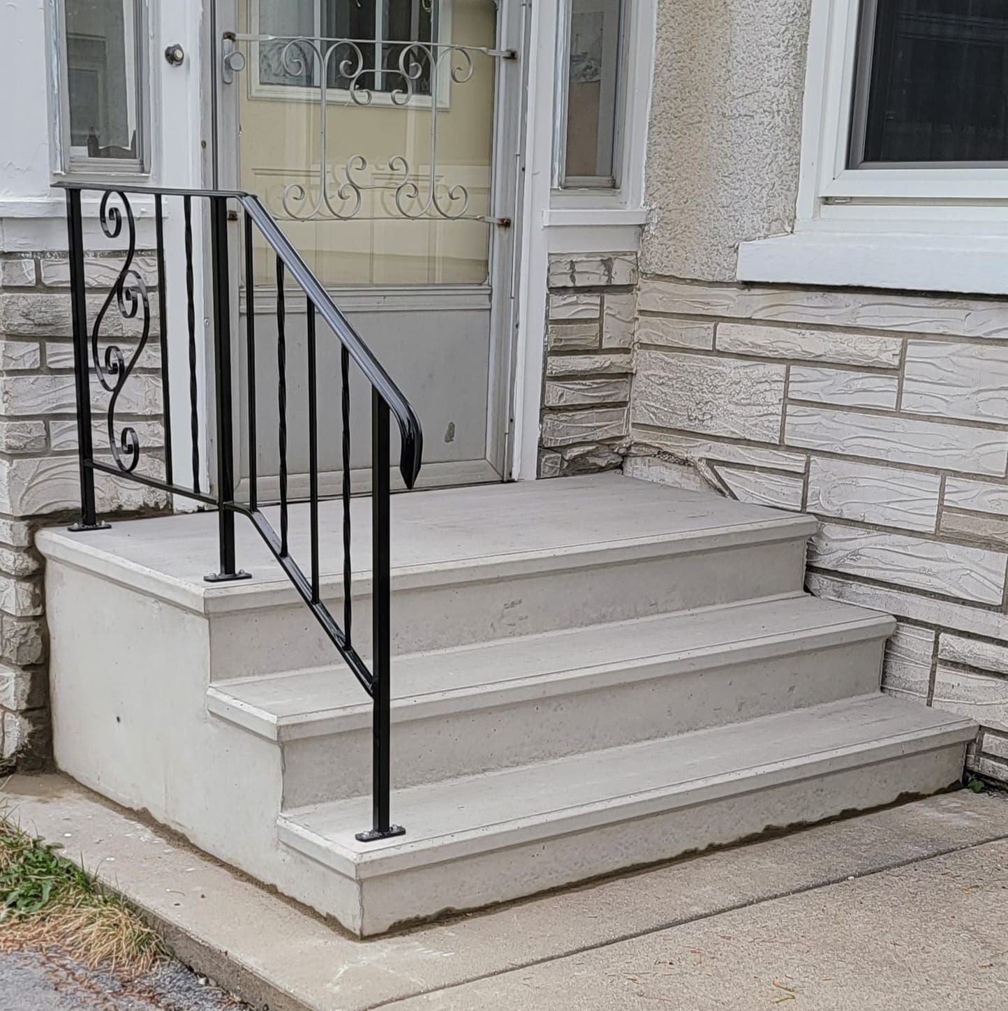 Front steps with a black metal railing leading to a white front door and stone-clad house facade