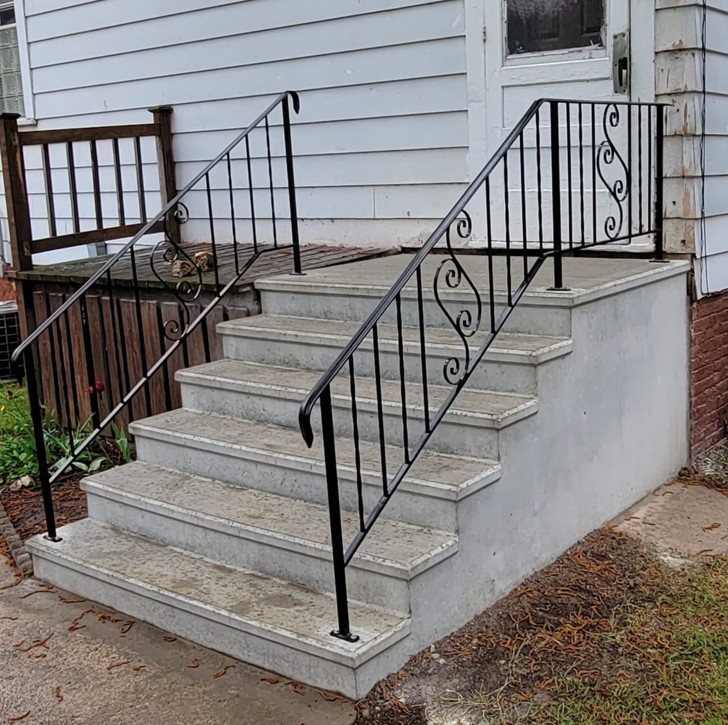 Concrete front steps with black wrought-iron railings leading to a white house entrance