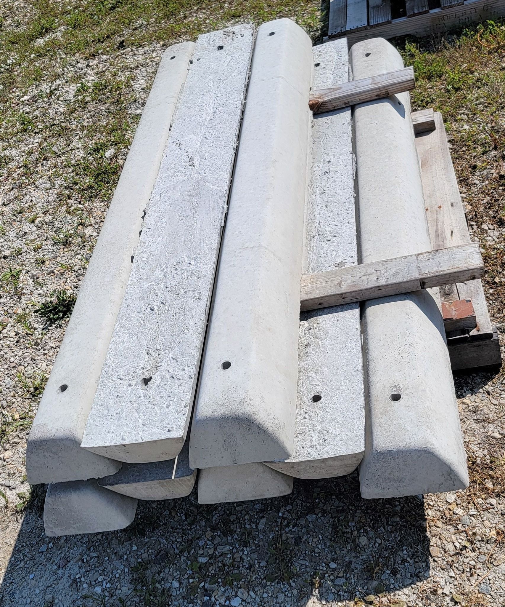 Stacked white concrete beams and blocks on gravel outdoors, with a few metal straps on top.