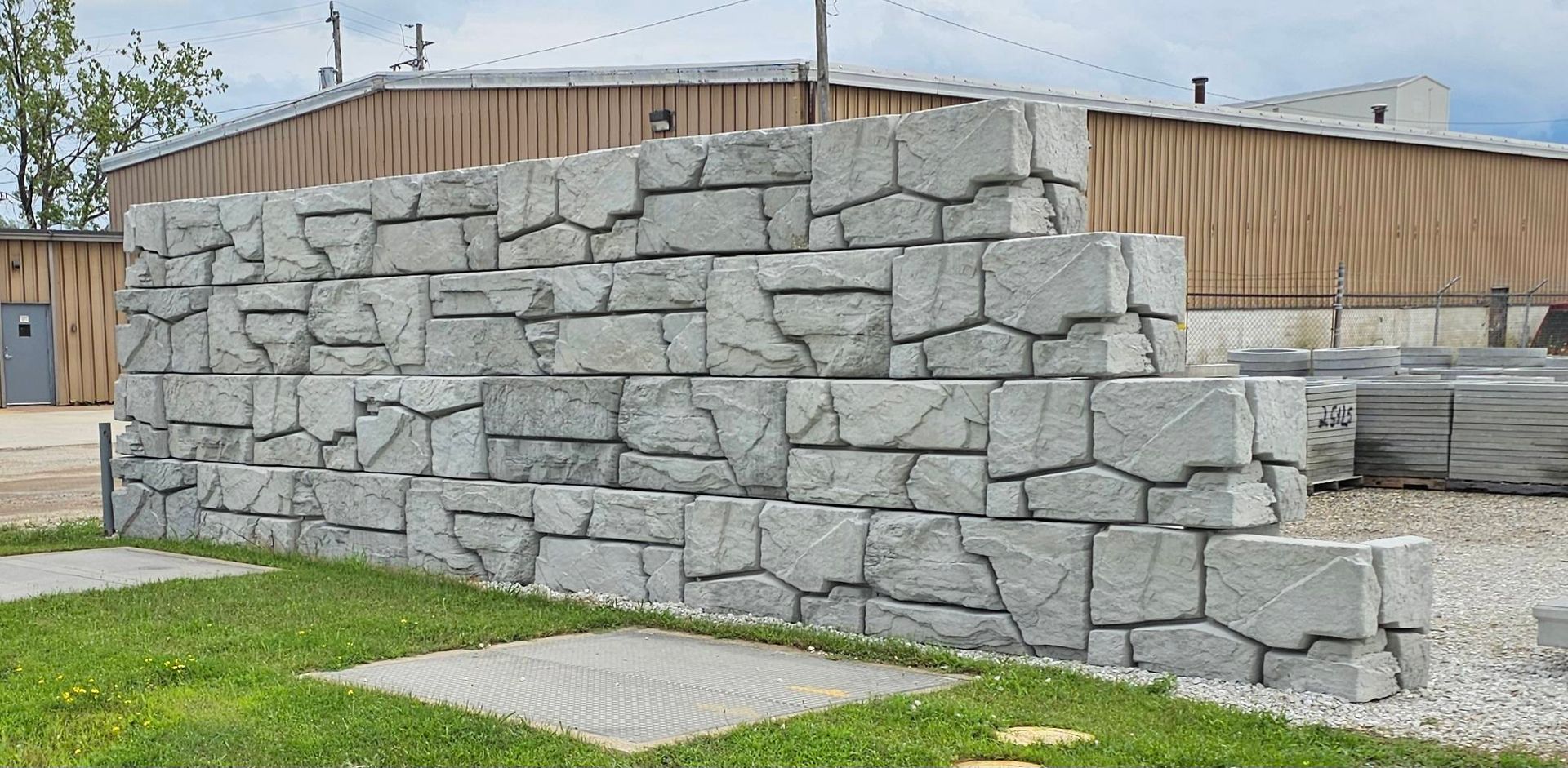 Gray stone retaining wall beside a grassy walkway in an industrial area