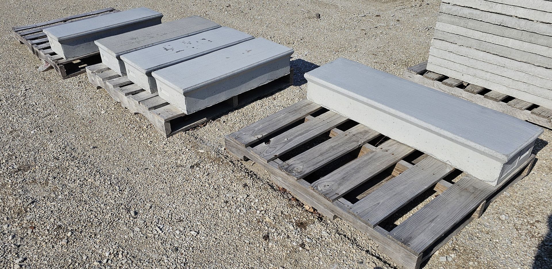 Stacked gray metal pallet racks and panels on gravel in bright sunlight