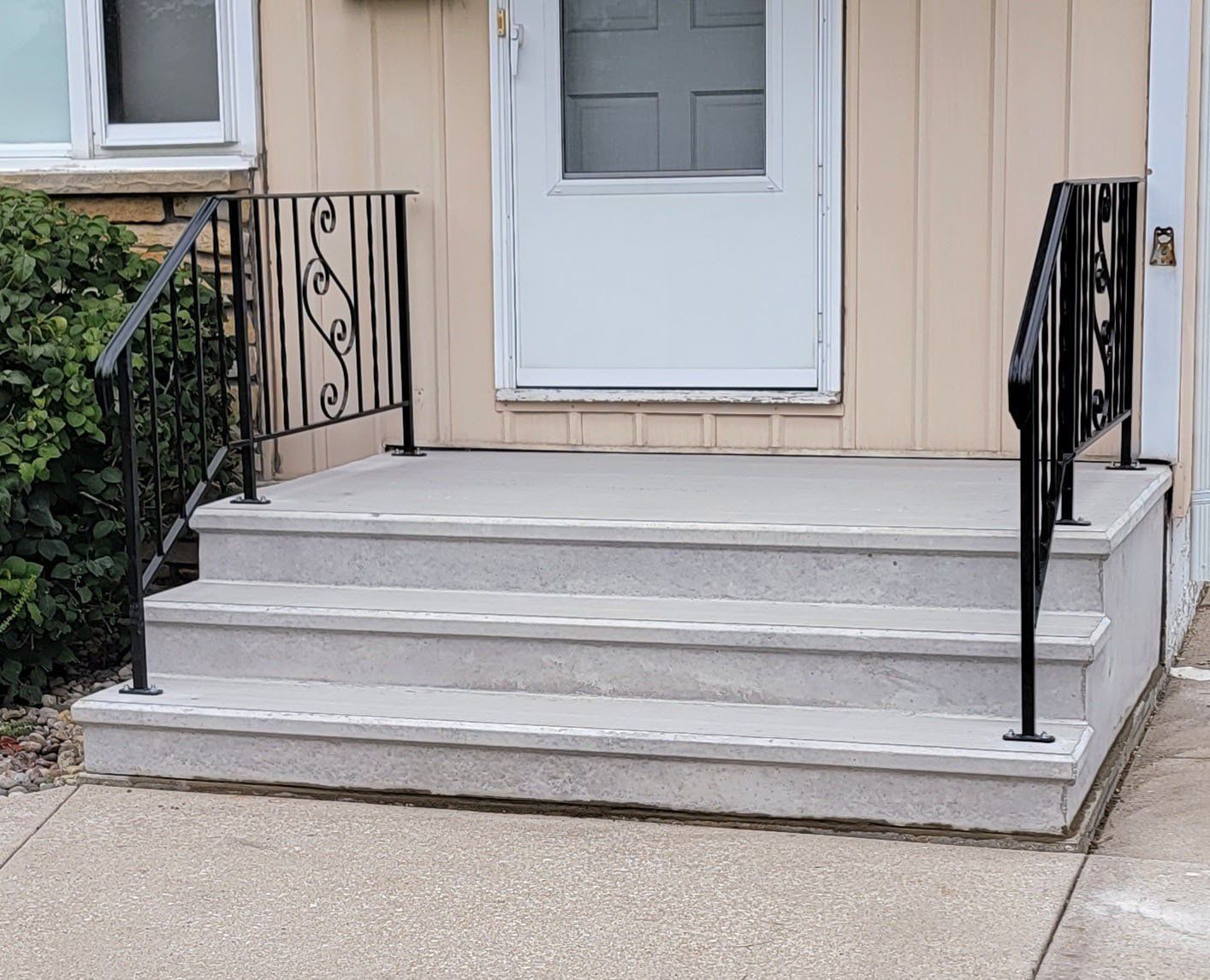 Front porch with white steps, black railings, and a white door on a beige house.