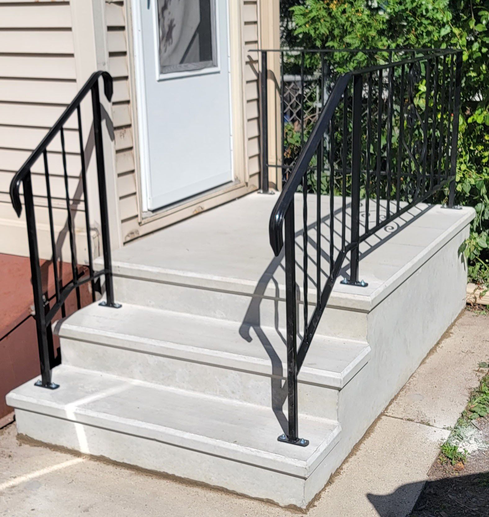 Front porch steps with black railings leading to a white door and beige siding.