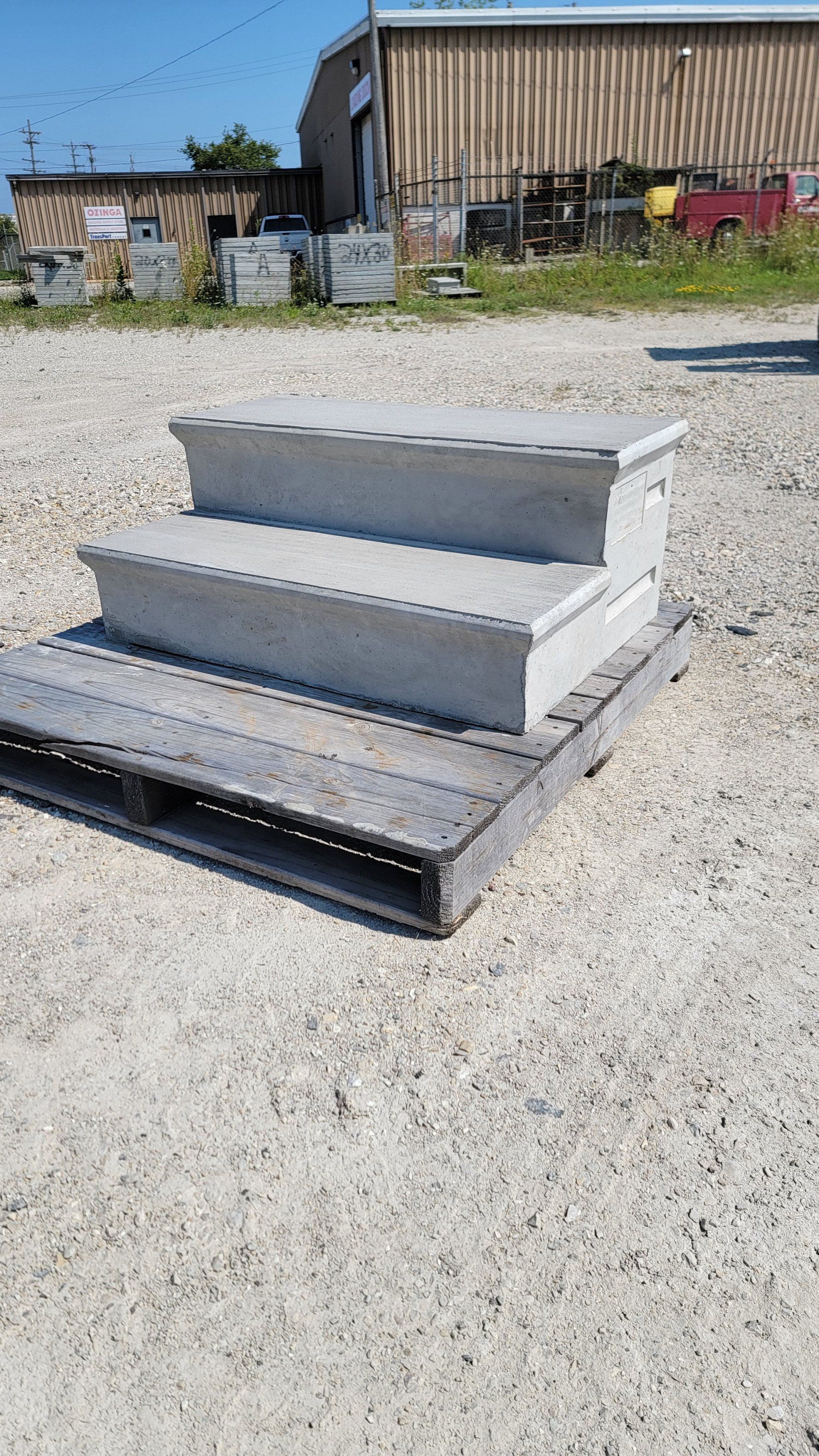Concrete steps and a metal ramp on gravel outside an industrial building.